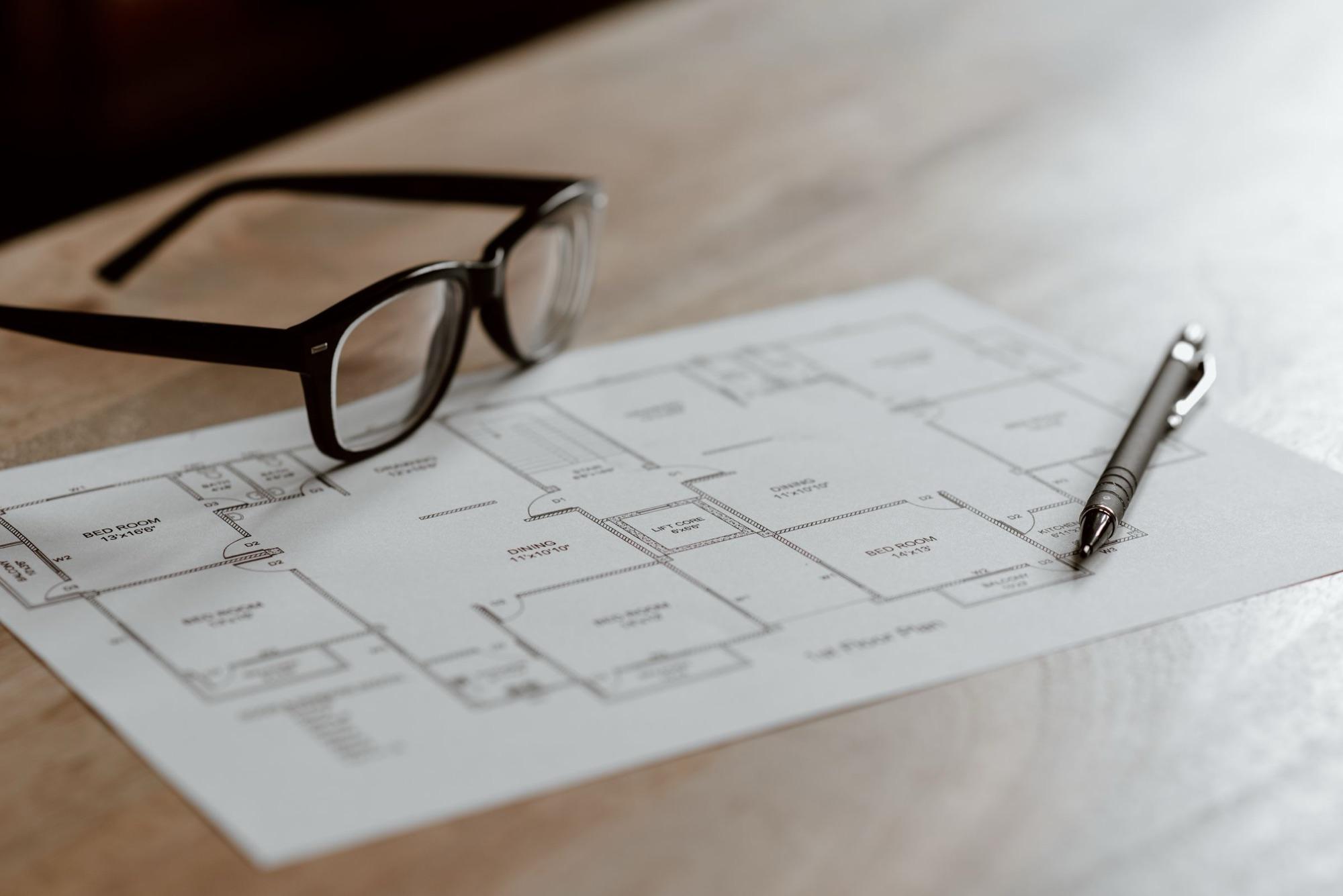 A floor plan on a table with reading glasses and a pen